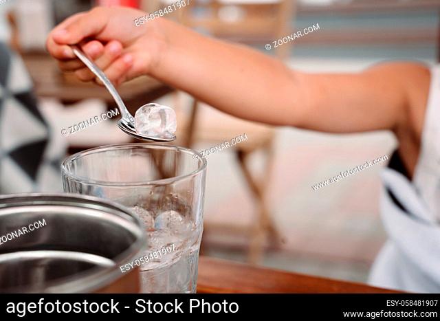 Little girl with mom playing with ice cubes in a cozy cafe. Good relationship of parents and child. Happy moments together