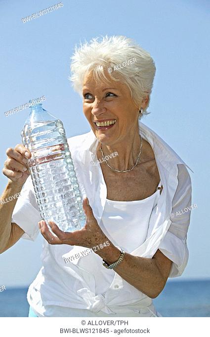 whitehaired woman at the beach drinking mineral water