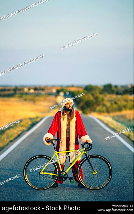 Man in Santa Claus costume standing with bicycle on road
