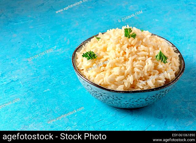 A bowl of rice, served with fresh parsley leaves, on a blue background with a place for text