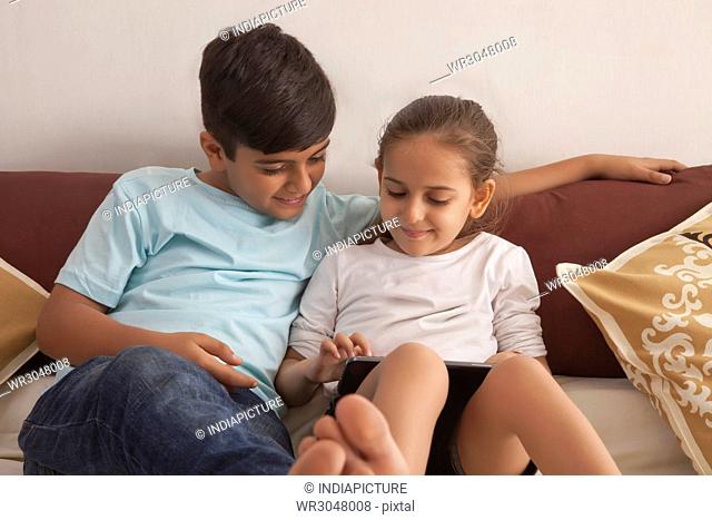 Brother and sister playing video game on digital tablet