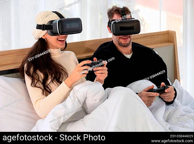 Happy couple wearing Virtual reality headset and having fun while playing VR games together in bed.. Gaming and technology concept
