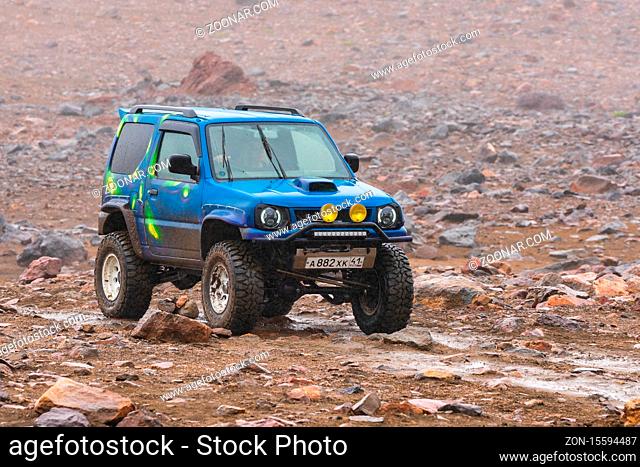 Japanese SUV Suzuki Jimny driving on rocky mount road on background volcanic landscape. Active vacation, travel destinations, off-road trip in rainy weather