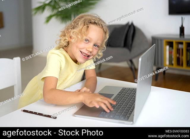Happy blond girl with laptop sitting at table in living room