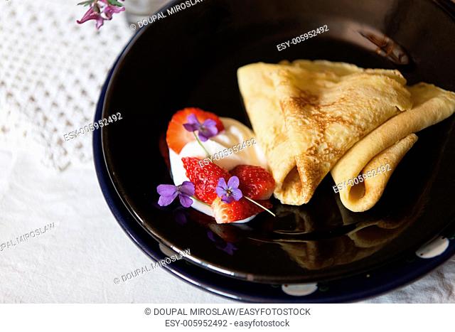 Pancakes with cut strawberries and cream on black plate on table covered with white napkin