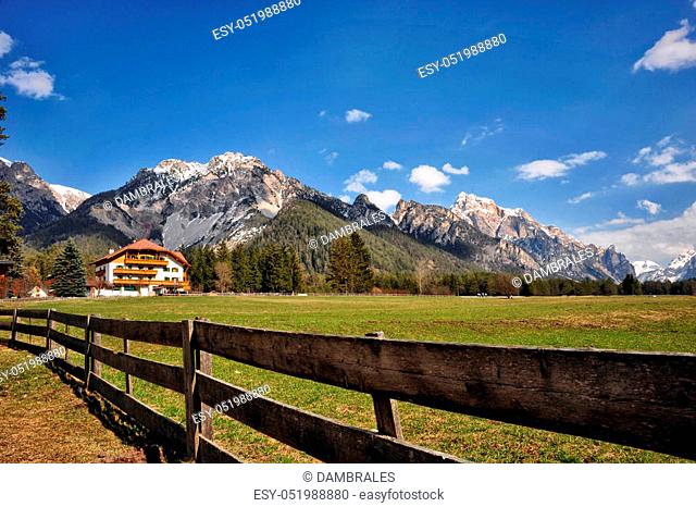 Landscape of Dolomites mountains in summer with a farm and meadows near a fence