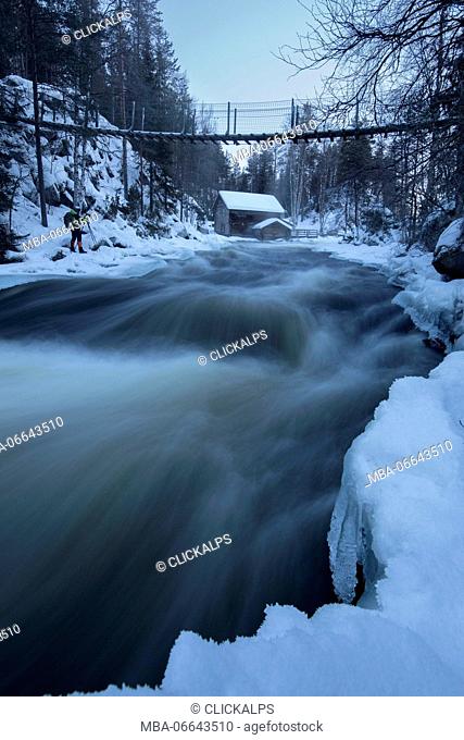 A wooden hut surrounded by the river rapids and snowy woods at dusk Juuma Myllykoski Lapland region Finland Europe