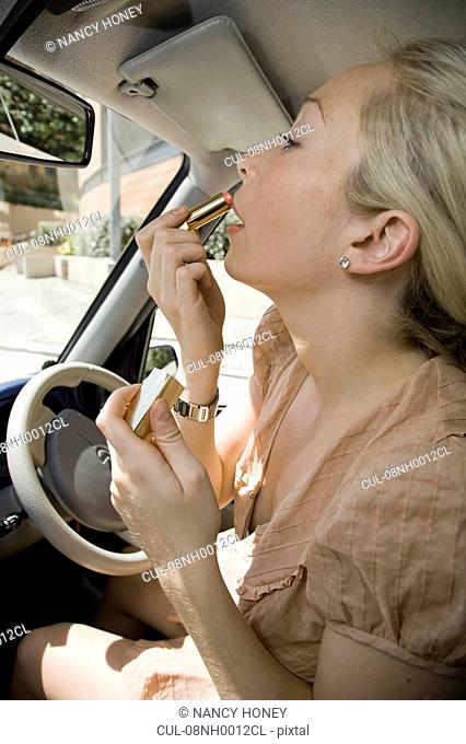 Young woman putting lipstick in car