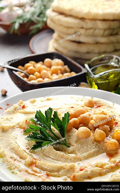 Low angle view at Hummus topped with chickpeas, olive oil and green coriander leaves on stone table with pita bread aside
