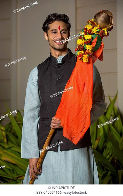Smiling maharashtrian man in traditional dress holding the gudi while celebrating gudi padwa festival
