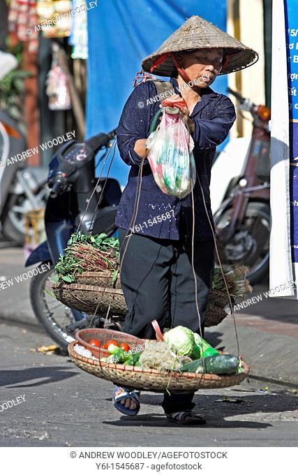 Woman in conical hat carrying shoulder pannier baskets of vegetables Hanoi Vietnam