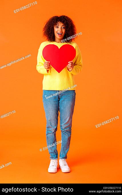 Full-length vertical shot lovely charismatic and dreamy african-american woman in sweater, jeans, holding big red heart as searching soulmate