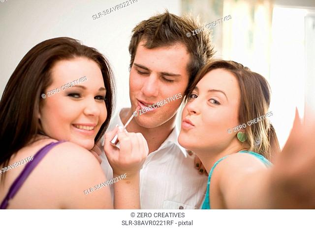 Teenage girls putting makeup on boy