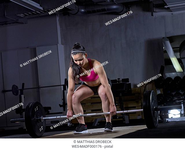 Young woman preparing for weightlifting with barbell
