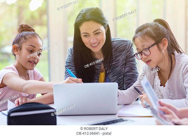Female teacher and girl students researching at laptop in library