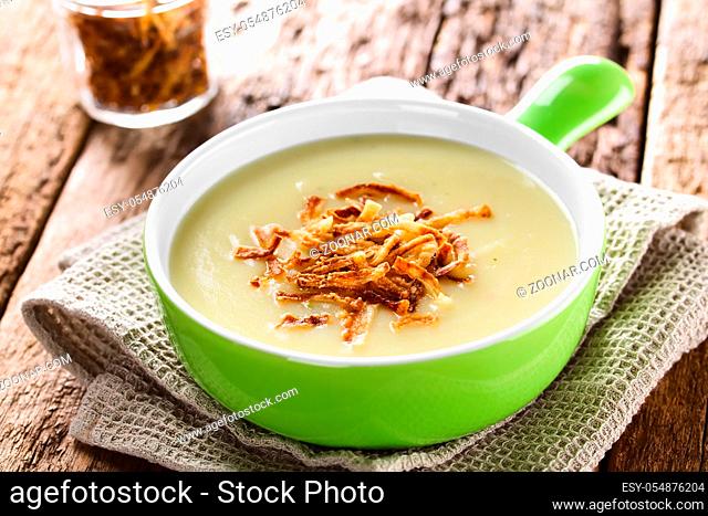 Fresh homemade cream of potato soup in green bowl garnished with crispy onion strings (Selective Focus, Focus one third into the bowl)