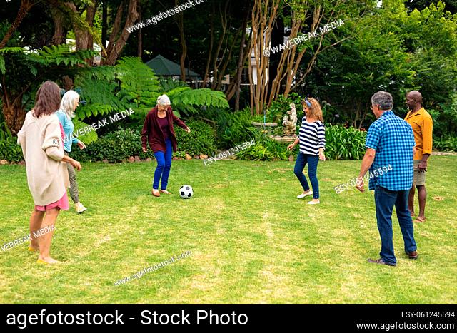 Multiracial active senior male and female friends playing soccer in backyard on weekend