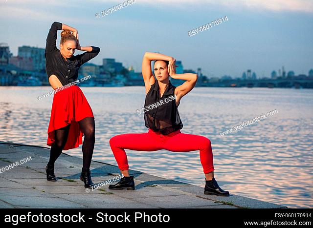 Two young beautiful twin sisters are dancing waacking dance in the city background near river. showing the different style and pose of modern dance with black...