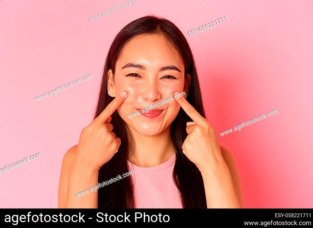 Beauty, fashion and lifestyle concept. Close-up of silly and cute, adorable asian girl poking her cheeks and smiling happily