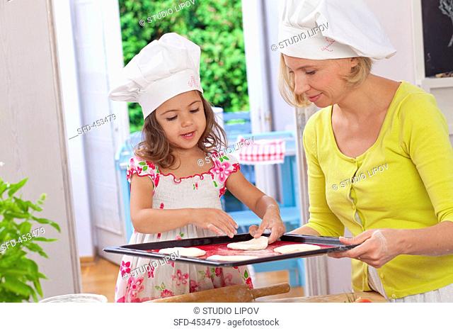 A mother and daughter placing pizza dough on a baking tray