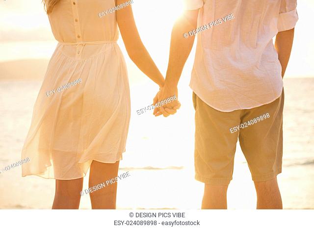 Couple holding hands at sunset on beach. Romantic young couple in love