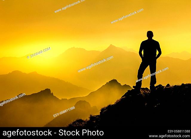 Relaxed man watching dreamfully towards sunrise and spectacular staggered mountain range silhouettes with bright back light