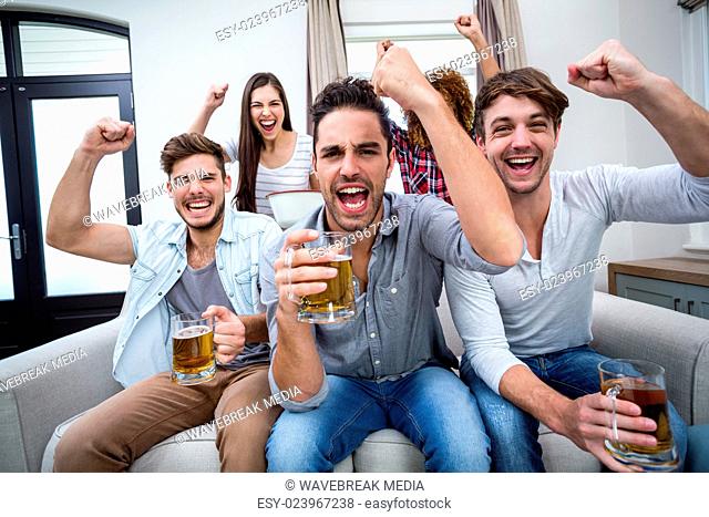 Friends cheering and drinking alcohol while watching soccer match