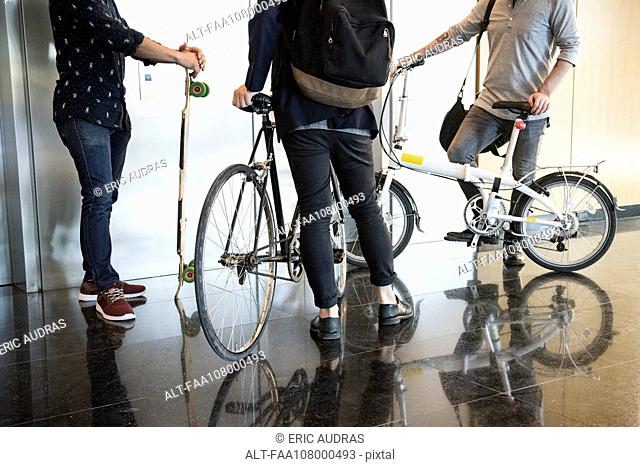 Men waiting for elevator with bicycles and longboard, low section