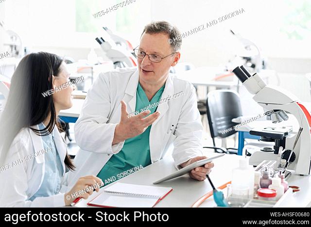 Teacher and student in white coats talking and using tablet in lab