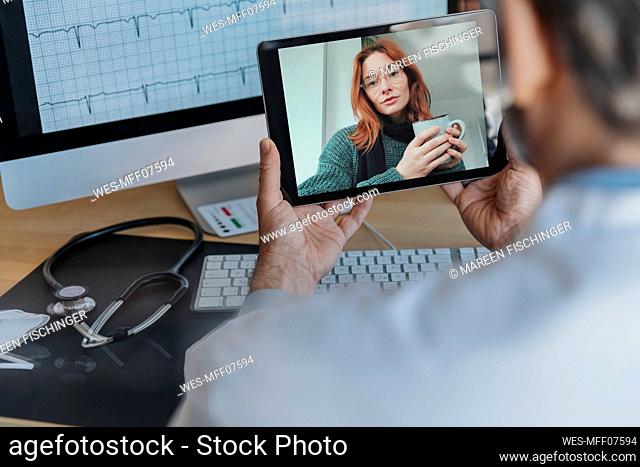 Male doctor talking to patient on video call over digital tablet while sitting at doctor's office