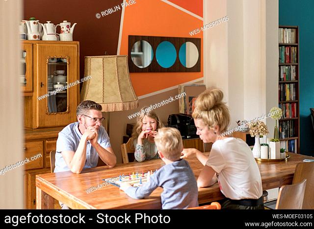 Family playing board game on dining table while sitting at home