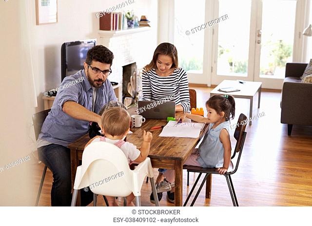Mother Uses Laptop Whilst Father Plays With Children At Home