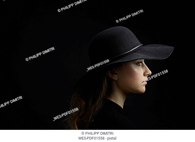 Profile of sad young woman wearing black hat against black background