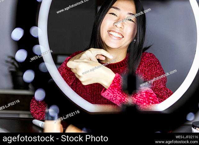 Cheerful female vlogger in front of illuminated ring light