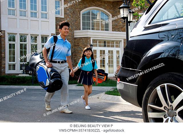 Oriental father and daughter standing by car with golf bag in front of villa