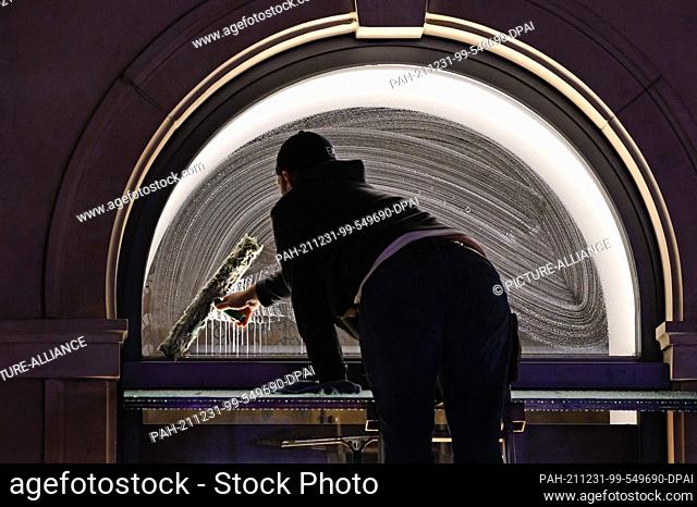 31 December 2021, Hamburg: A man cleans the façade and windows of a shop on Jungfernstieg in the early morning. Photo: Jonas Walzberg/dpa