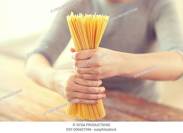 cooking, food and home concept - close up of female hands holding uncooked spaghetti pasta
