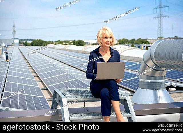 Senior businesswoman sitting with laptop at rooftop with solar panels