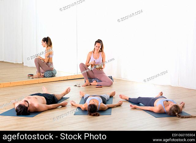 Yoga instructor and group of young sporty people in yoga studio, lying and relaxing on yoga mats during restorative yoga session