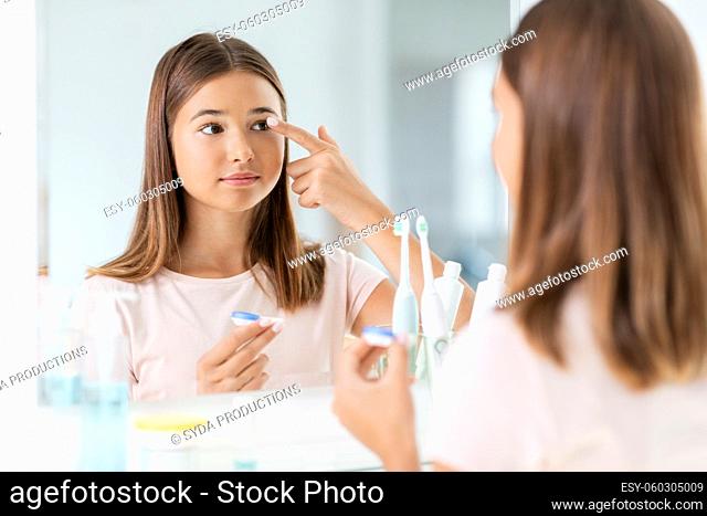 teenage girl applying contact lenses at bathroom