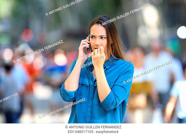 Nervous woman biting nails while is talking on phone on the street