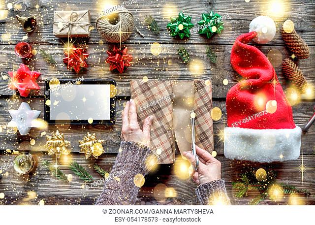 Christmas. A woman is preparing a New Year's gift. Set with Christmas objects and a tablet computer on a wooden background