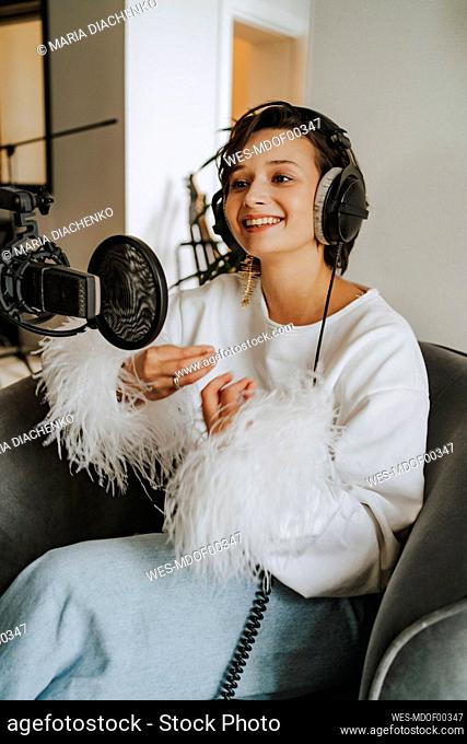 Smiling musician wearing headphones recording podcast through microphone in studio