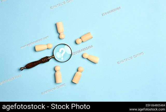 Wooden men and a magnifying glass on a blue background. Recruitment concept, search for talented and capable employees, career growth, flat lay