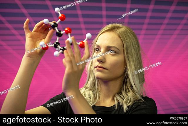 Close-up of female scientist holding molecule model against grid pattern
