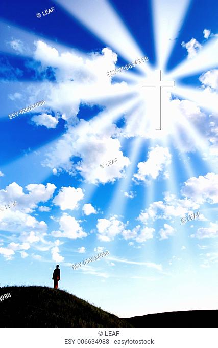 A person on a hill looking up to a glowing cross in the sky