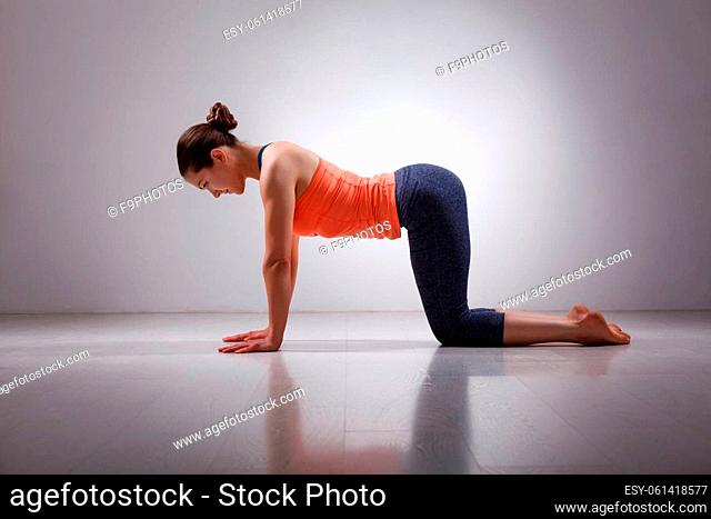 Beautiful sporty fit yogini woman practices yoga asana bitilasana - cow pose gentle warm up for spine (also called cat-cow pose) in studio