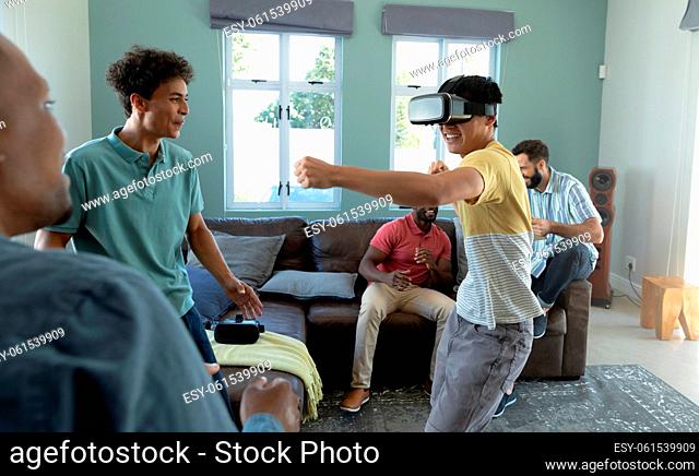 Multiracial playful young man wearing virtual reality simulator punching friends in living room