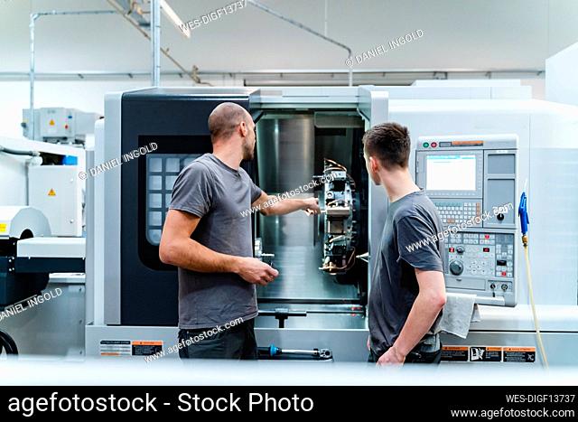 Engineer showing machine part to trainee while working at industry