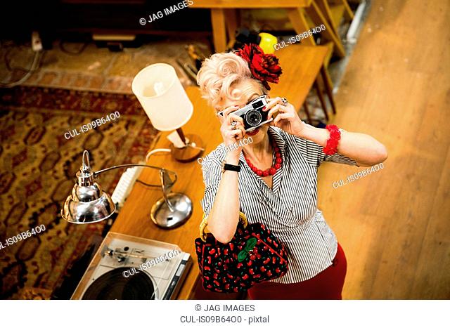 Quirky woman taking photographs on vintage camera in antiques emporium